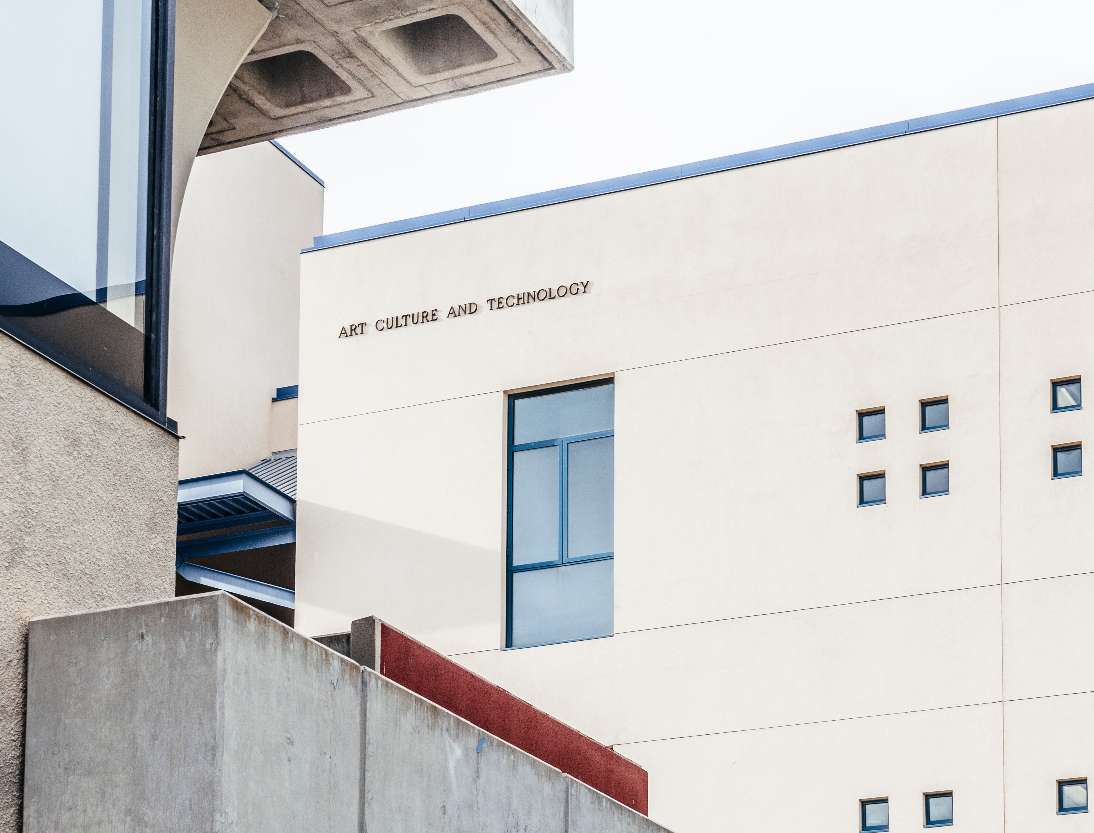 A building exterior displays the words “ART, CULTURE, AND TECHNOLOGY” on a light-colored wall. Clean architectural lines, a blue-framed window, and concrete elements frame the modern facade.