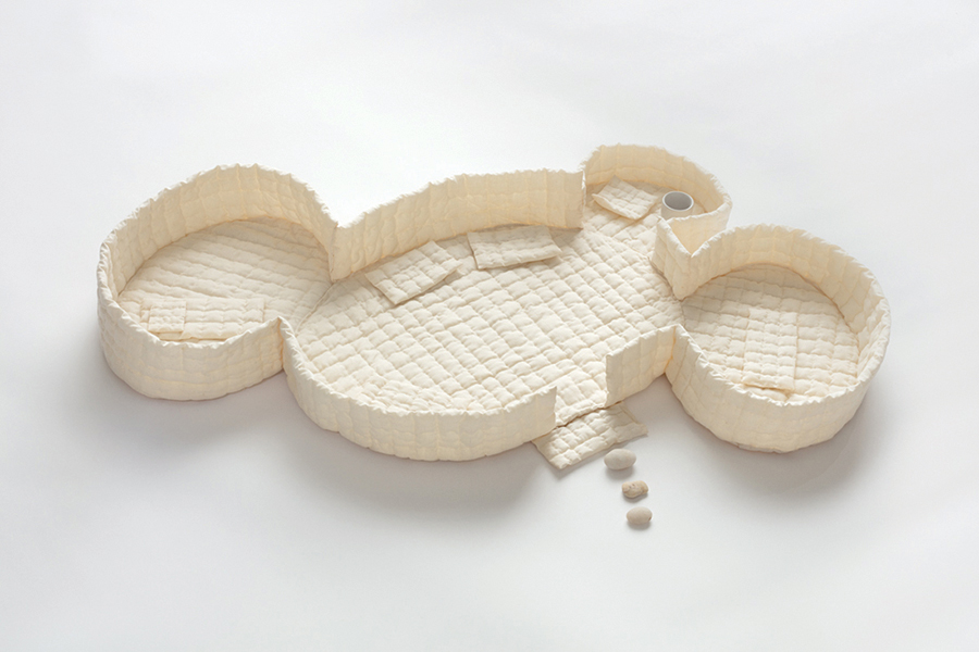Abstract cream-colored sculptural object composed of connected circular and rounded compartments with textured interior surfaces, placed against a plain background.
