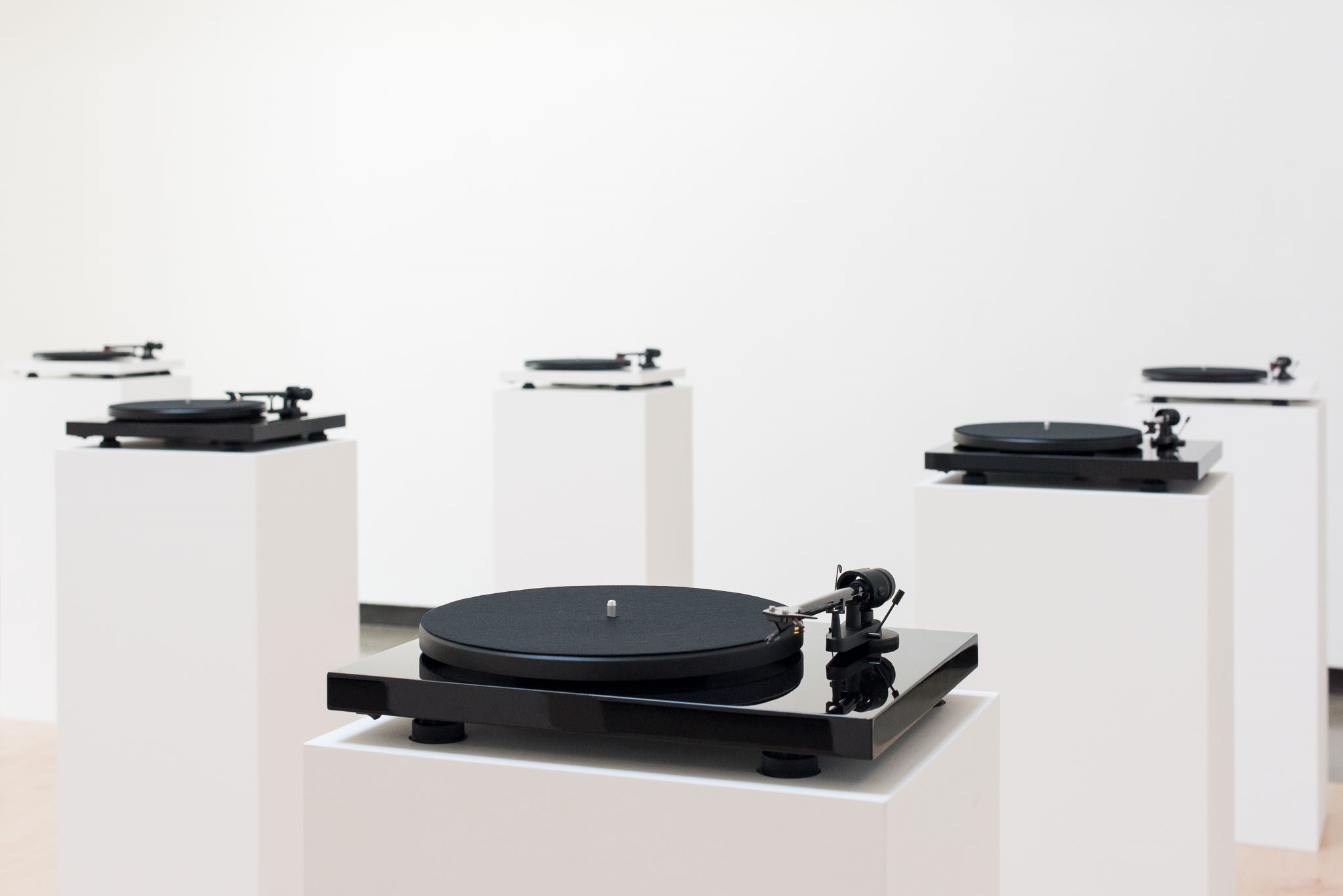 Several turntables displayed on white pedestal stands against a plain gallery wall.