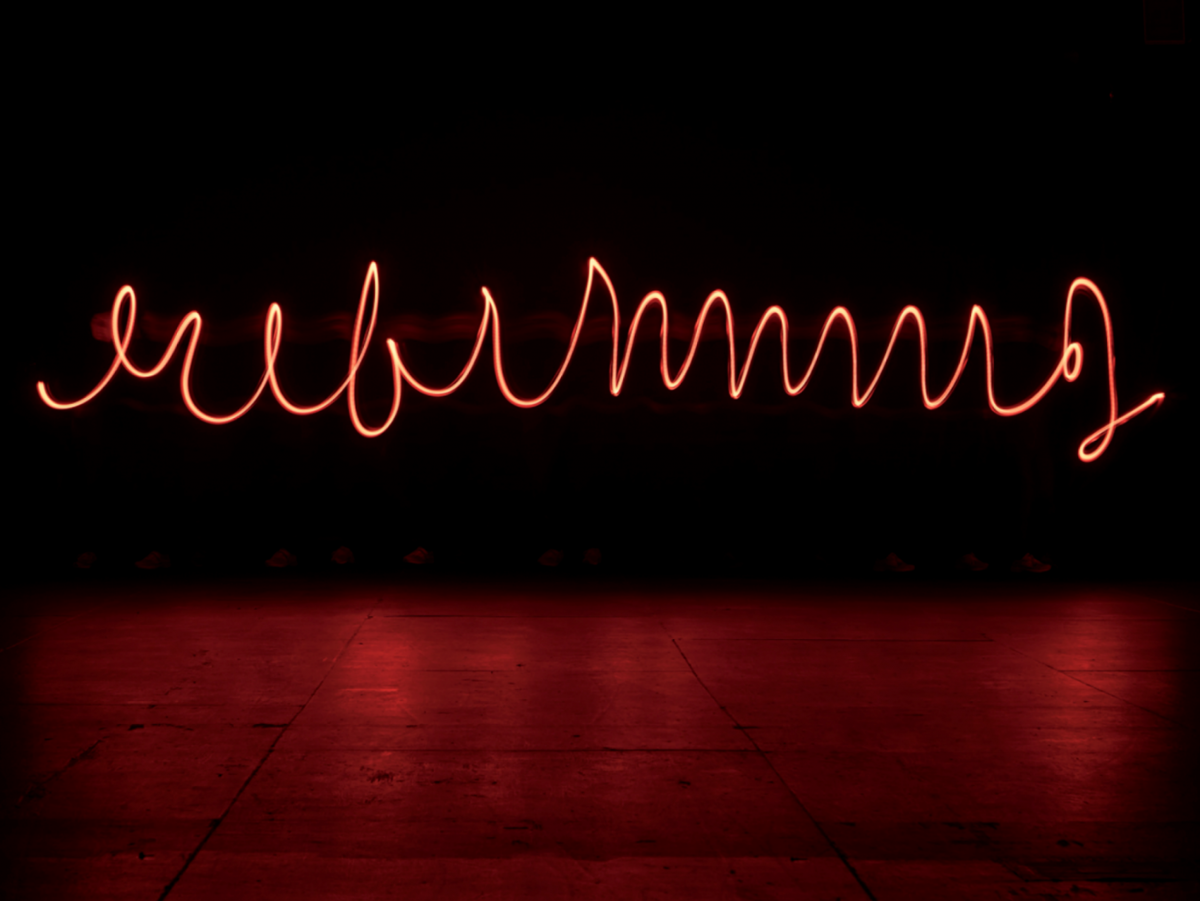 Red neon light spelling a word in cursive against a dark background, glowing above a reflective floor.