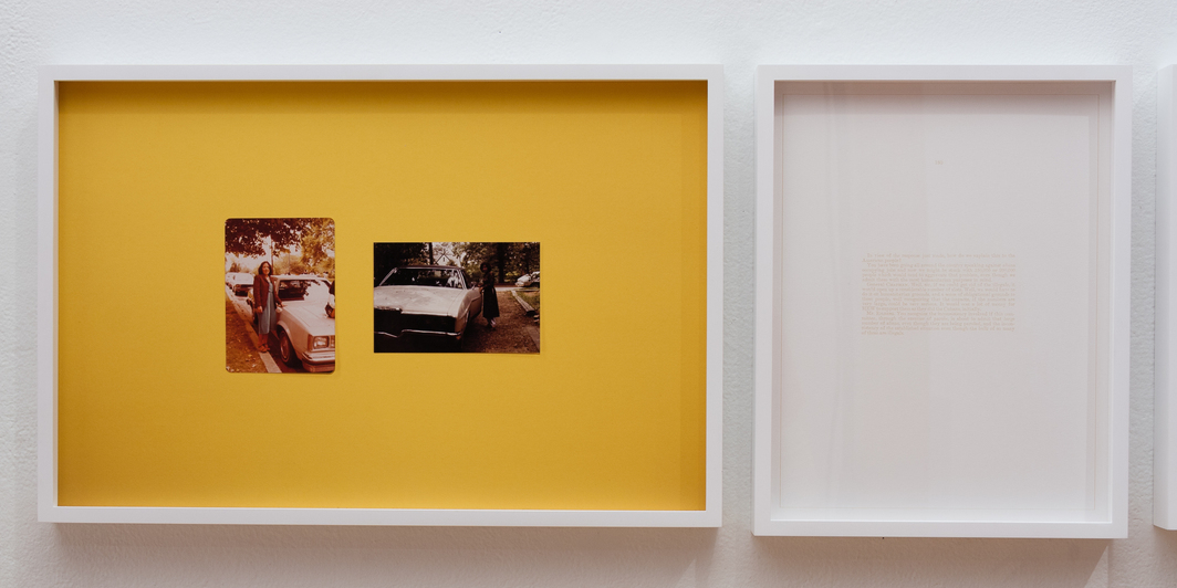 White-framed display with a mustard-yellow background holding two small photographs side by side, while an adjacent empty white frame hangs to the right on a white wall.