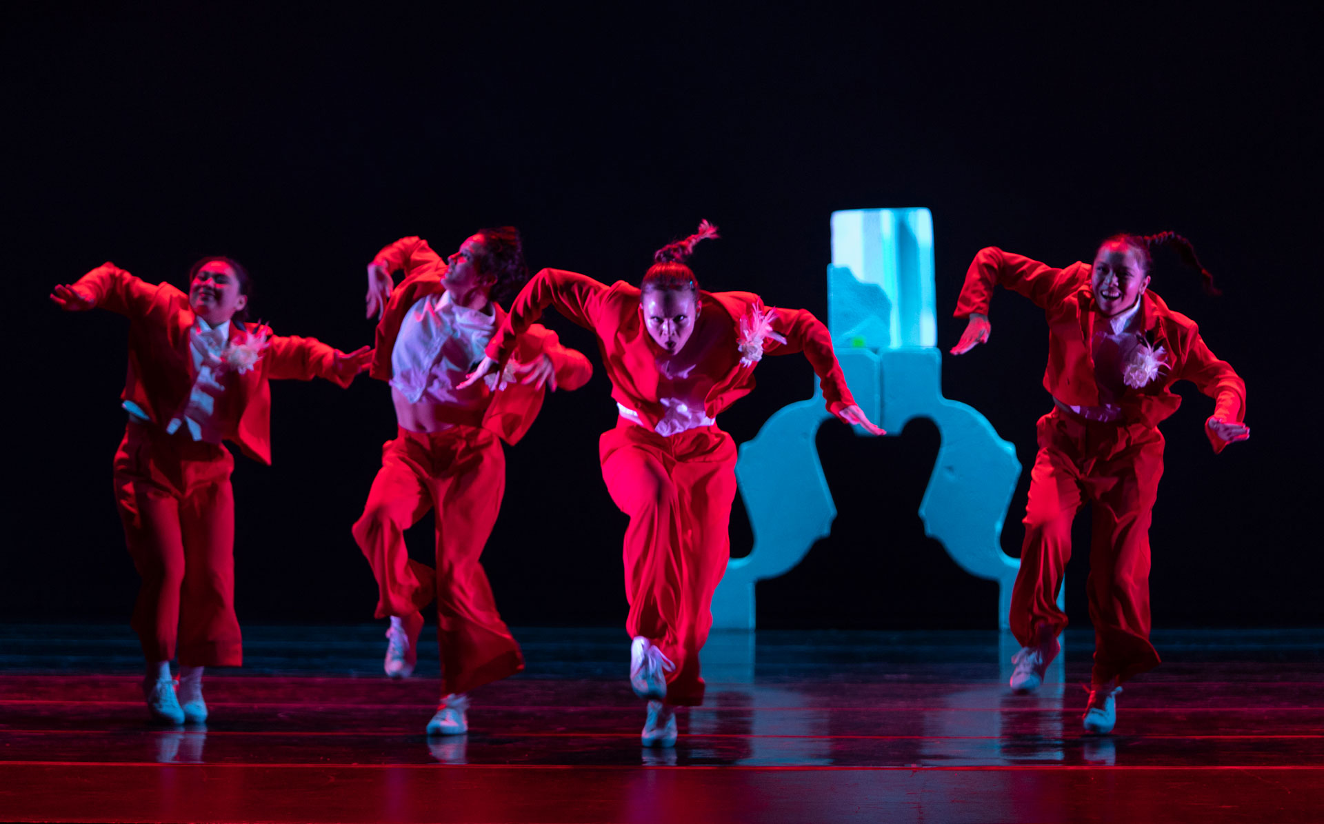 Students perform a hip-hop dance in red suits during Dance Visions 2024, moving energetically across a stage under dramatic lighting.