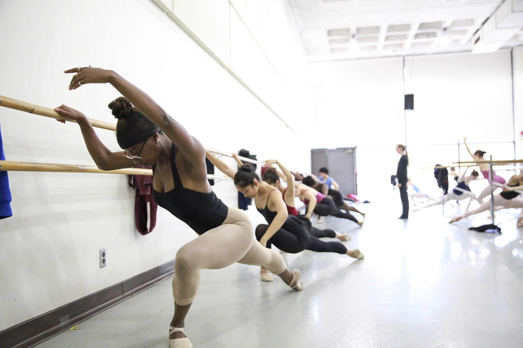 Students practice ballet exercises at the barre in a bright dance studio.
