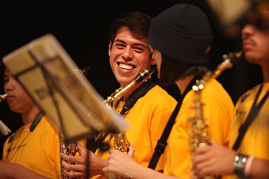 Members of the UCI Athletics Band play saxophones together, smiling and performing in matching yellow shirts.
