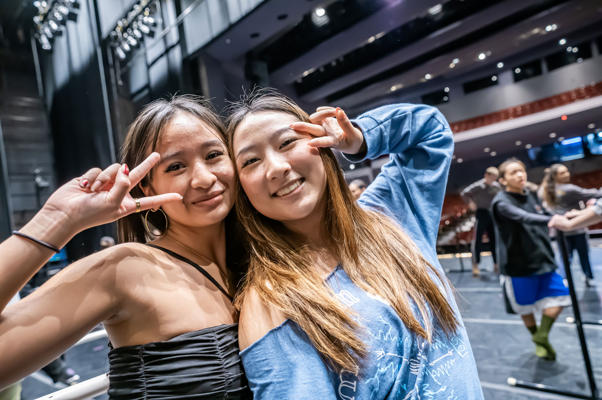 Two dancers smile on stage of the Irvine Barclay Theatre making the peace sign