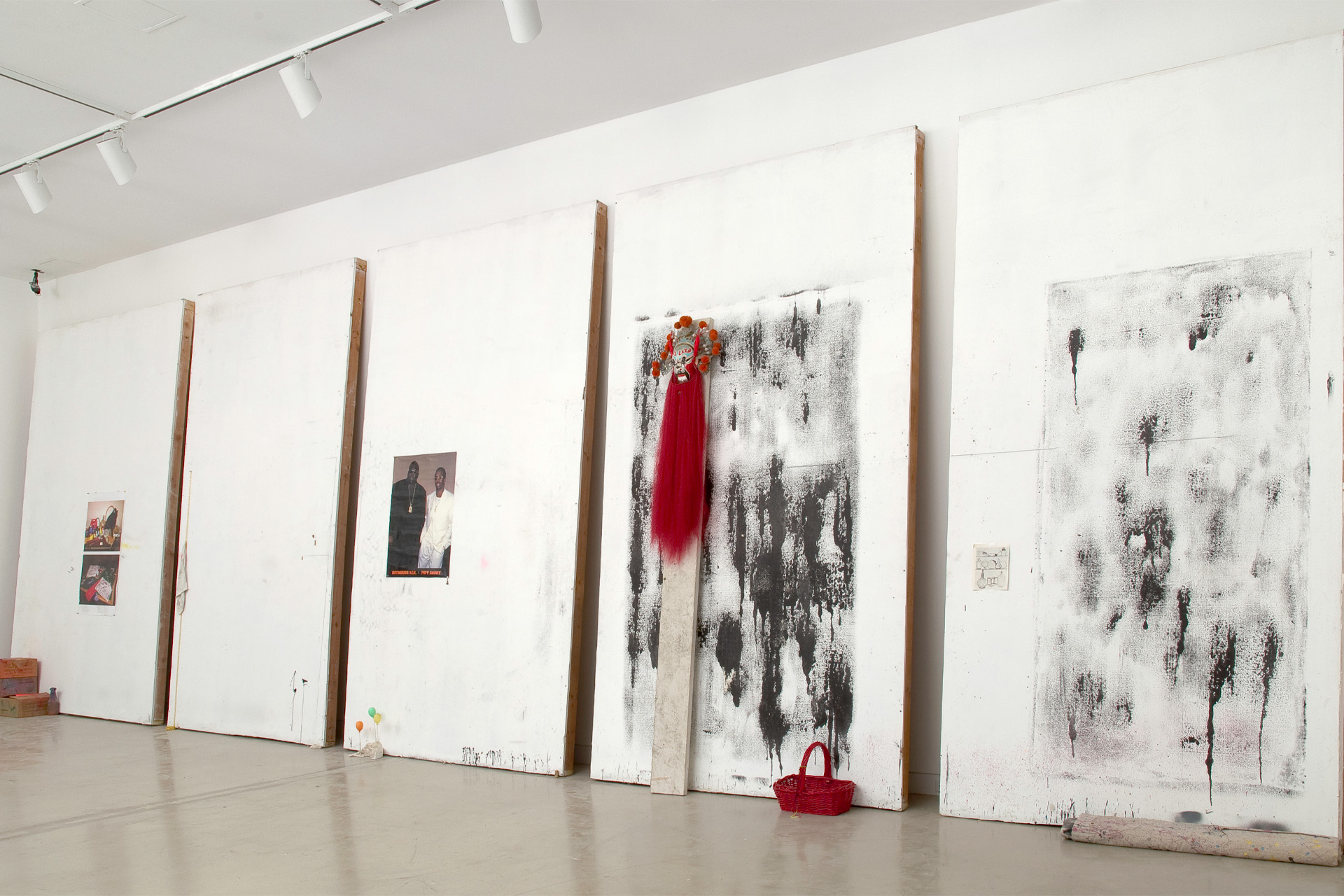 White gallery wall displaying large abstract black-and-white paintings mounted on wooden supports, with a red garment and red handbag incorporated into the installation.