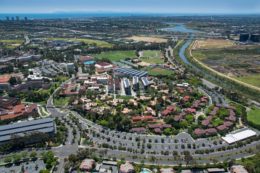 Aerial view of the UC Irvine campus showing academic buildings, green spaces, roads, and surrounding waterways.