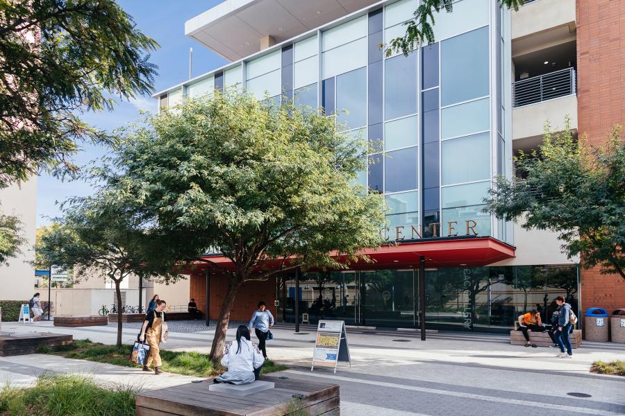 Exterior view of the Contemporary Arts Center with glass facade, trees, and students gathering in the plaza outside.