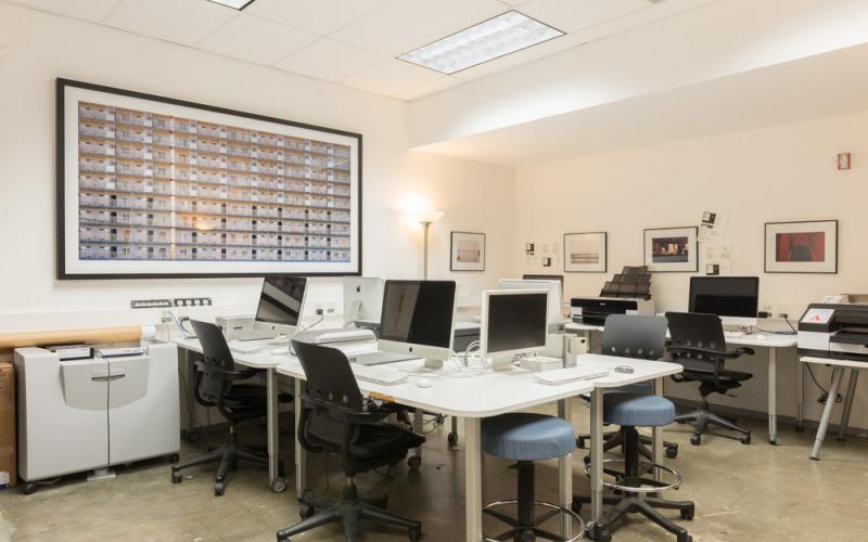 A computer lab with desktop workstations, printers, and framed artwork lining the walls.