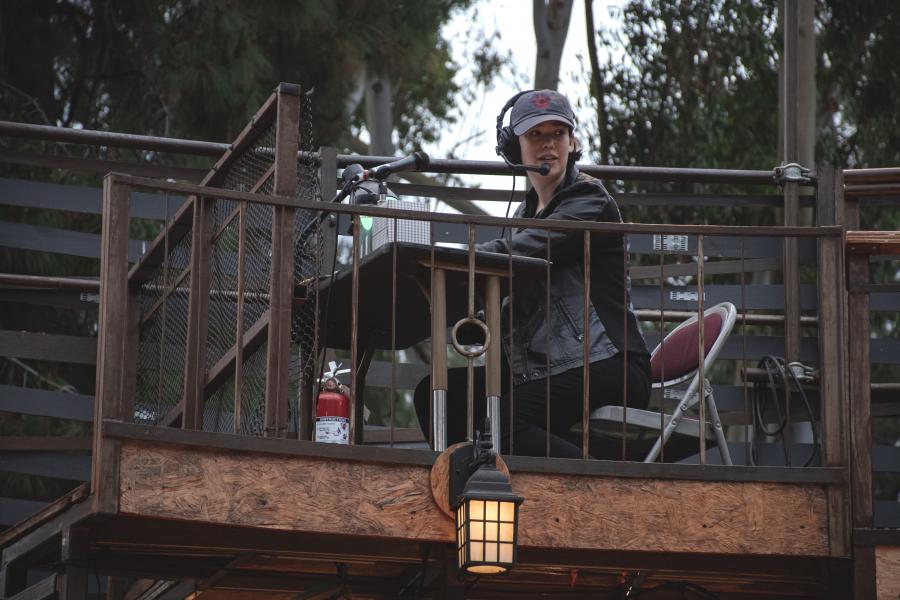 A stage manager wearing a headset operates sound or cues from a raised booth during an outdoor theatrical production.