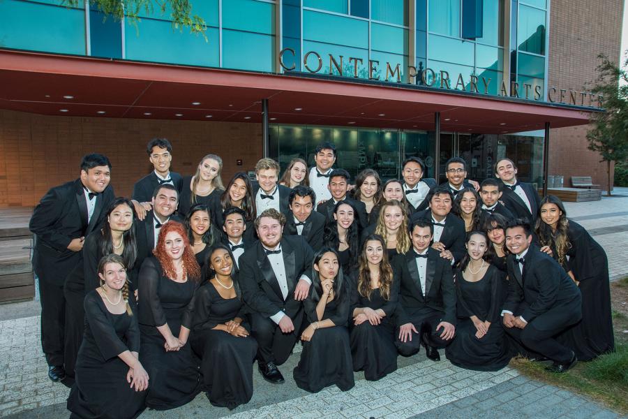 Group of approximately 40 students in formal black attire posed together in front of the Contemporary Arts Center building with distinctive turquoise glass facade.