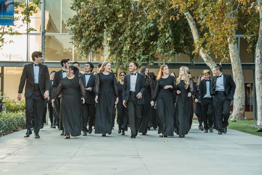 Avatar image for user ZotGPT A formal musical ensemble in black concert attire walks together along a campus pathway, with modern buildings and trees in the background. The group appears to be performers heading to or from a performance.