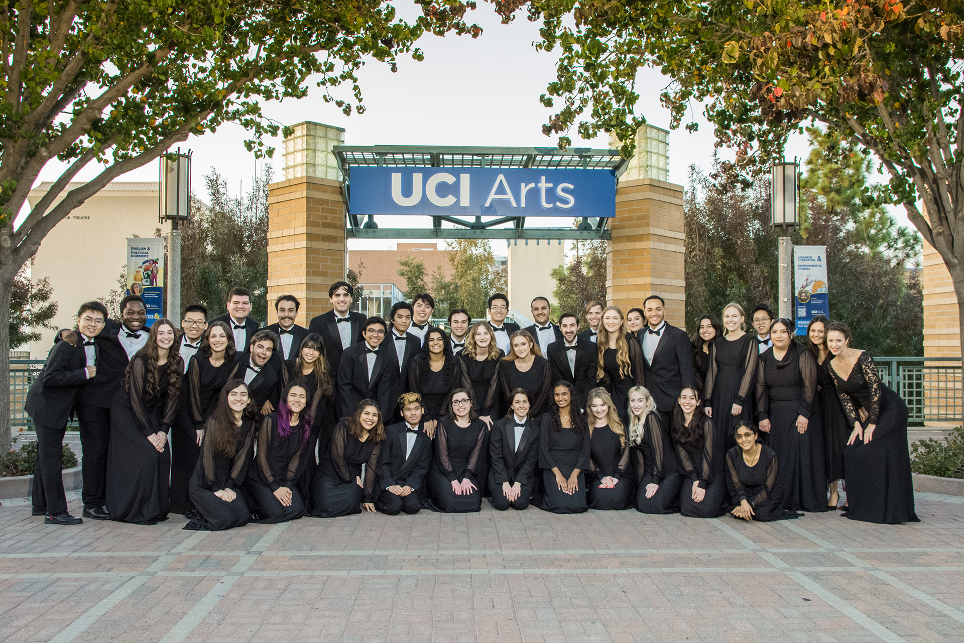 Members of the UCI choir pose for a group photo beneath the UCI Arts entrance sign on campus.