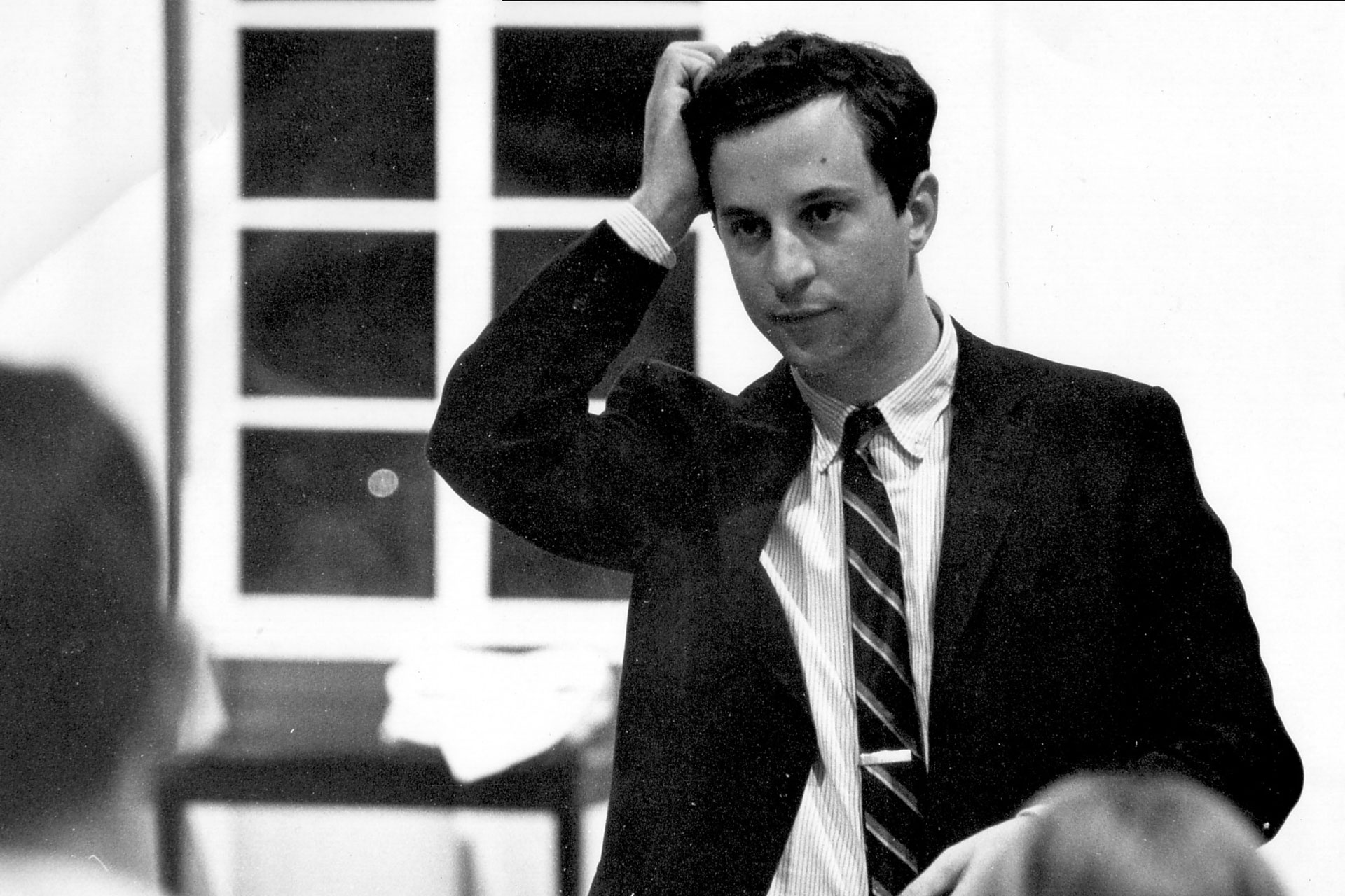Robert Cohen, archival black-and-white photograph of a man in a suit speaking in an indoor setting, captured mid-gesture.