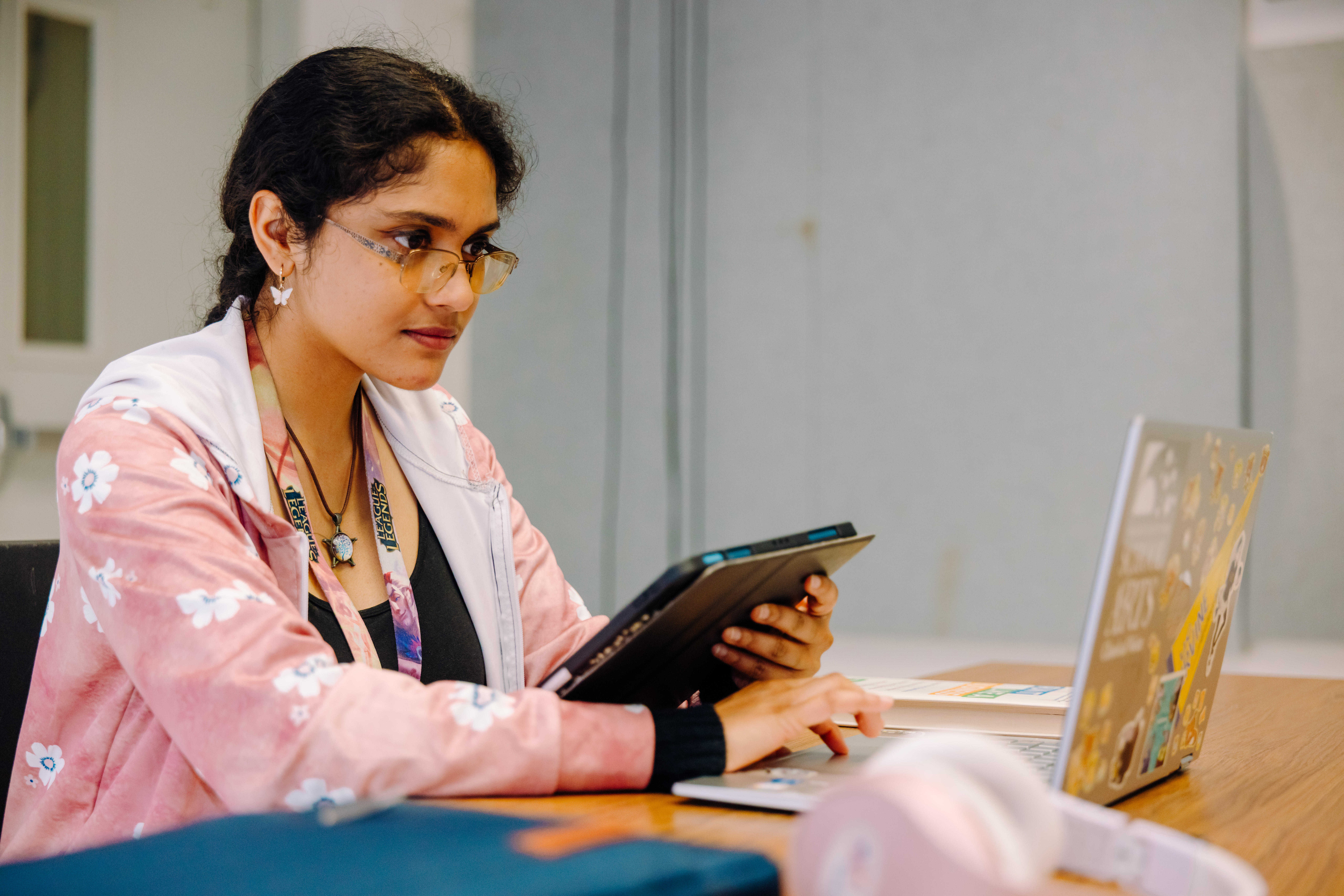 A UCI Arts student working on a laptop at a desk while holding a tablet. 