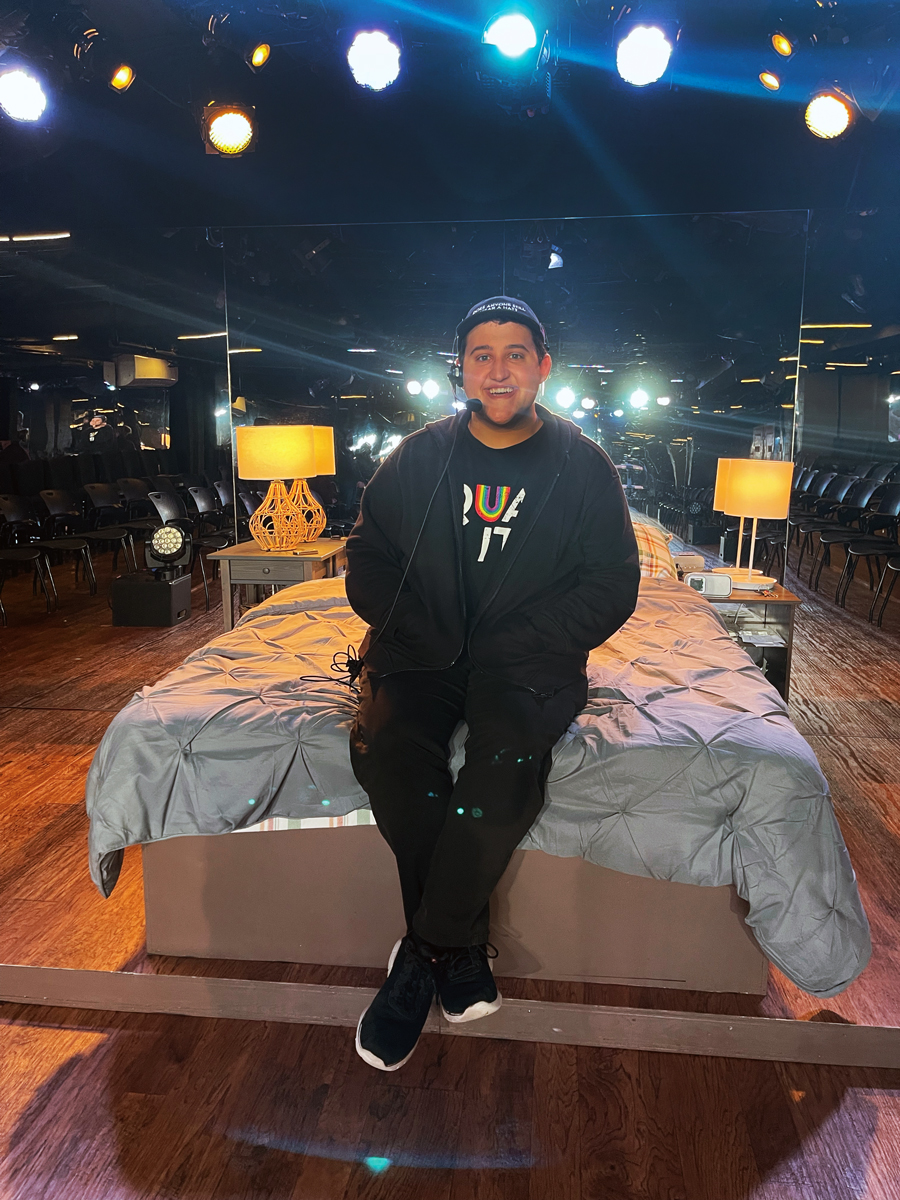 UCI Drama student seated on a bed set under stage lighting, preparing or performing in a theater production