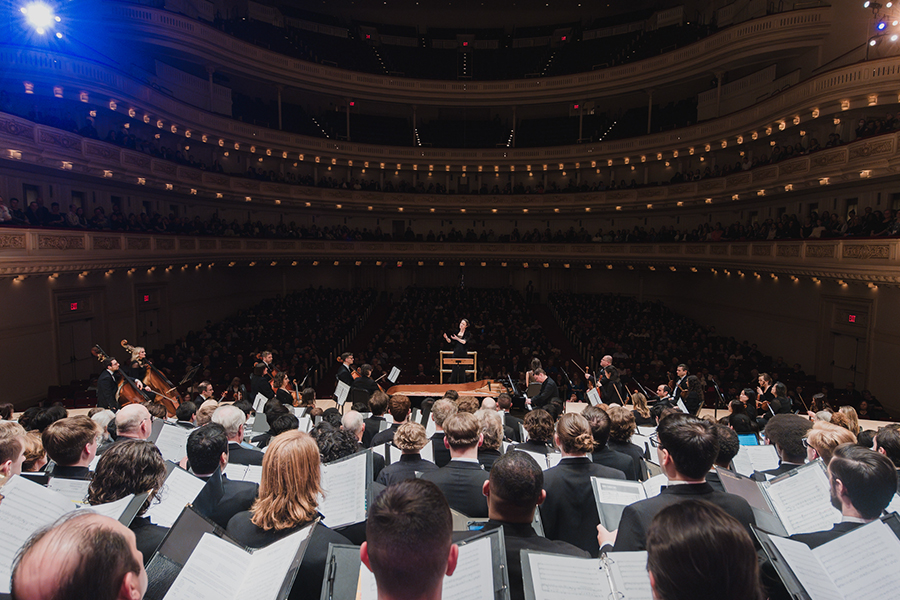 Image: Irene Messoloras conducting with choir and orchestra that includes members of  UCI Chamber Singers at Carnegie Hall. Photo by DCINY Production/Dan Wright photography.