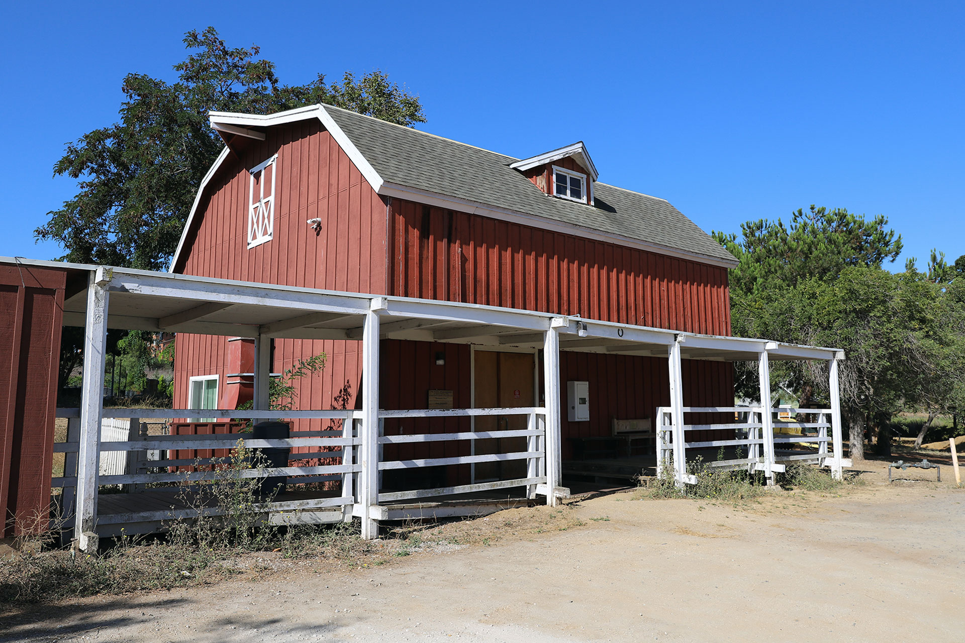 The Growtoski Barn. A barn-style building with covered porch and white railings on a campus or outdoor site, set against a clear blue sky.