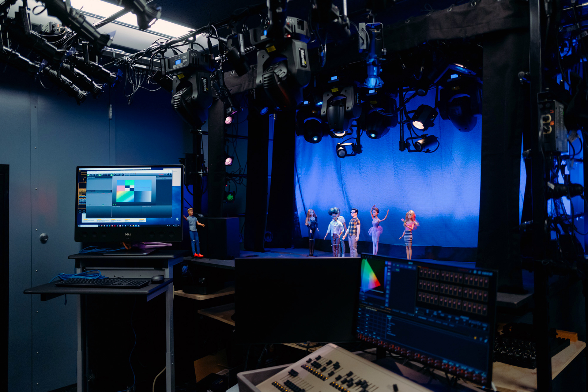 Performance technology lab with overhead stage lighting and digital control systems illuminating puppet figures arranged on a small stage