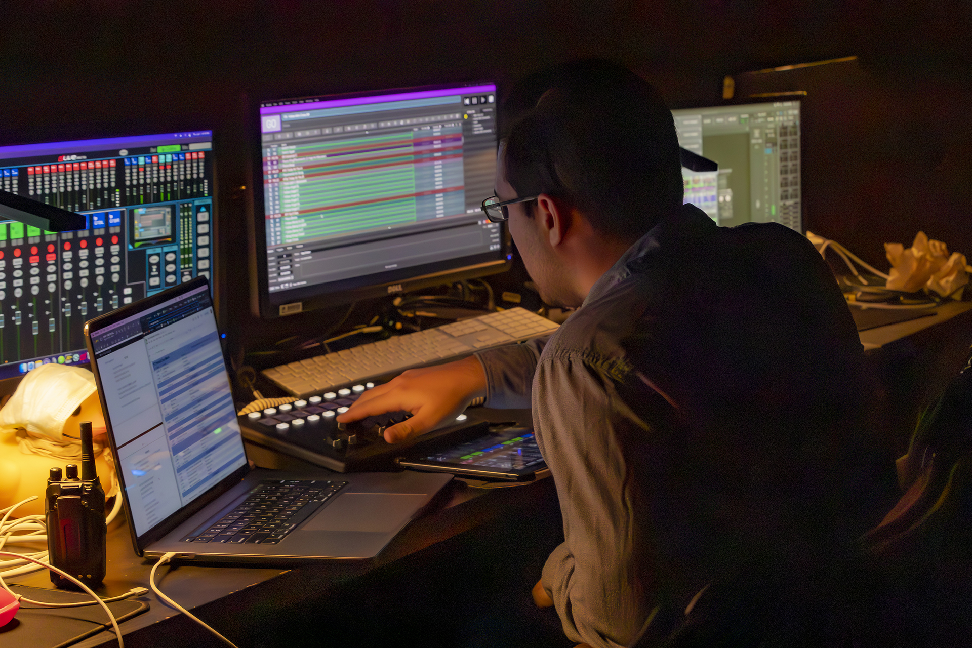 Student adjusts controls while monitoring digital production software across multiple screens in a production workspace