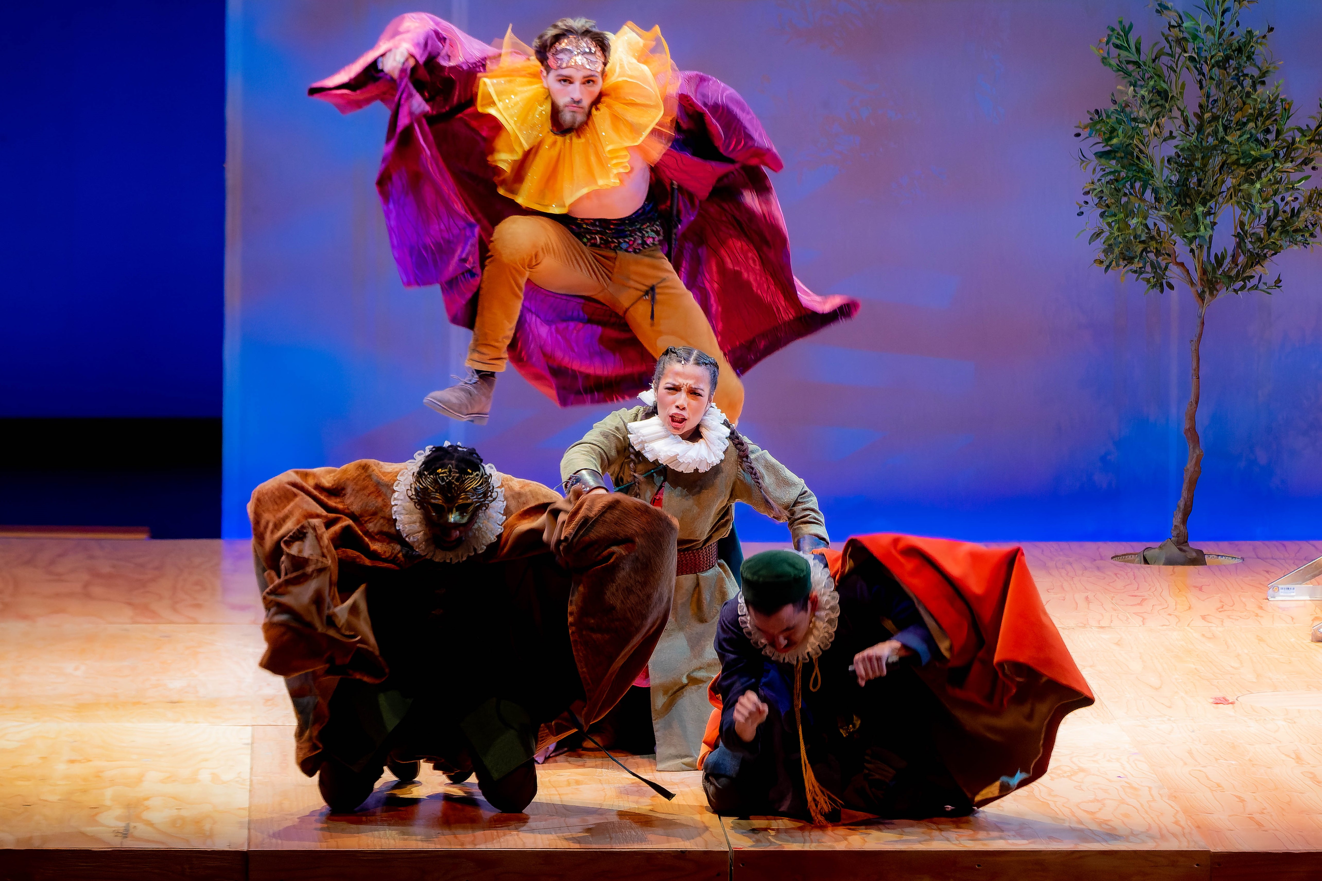 UCI Drama students perform a dramatic, movement-driven scene on stage, featuring bold costumes and expressive physical action