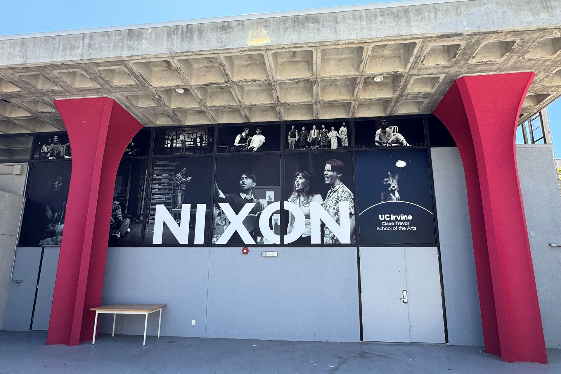 Front exterior of the Nixon Theatre at UC Irvine Claire Trevor School of the Arts, featuring bold red columns, black-and-white theatrical production imagery across the windows, and large “NIXON” lettering beneath a concrete overhang on a sunny day