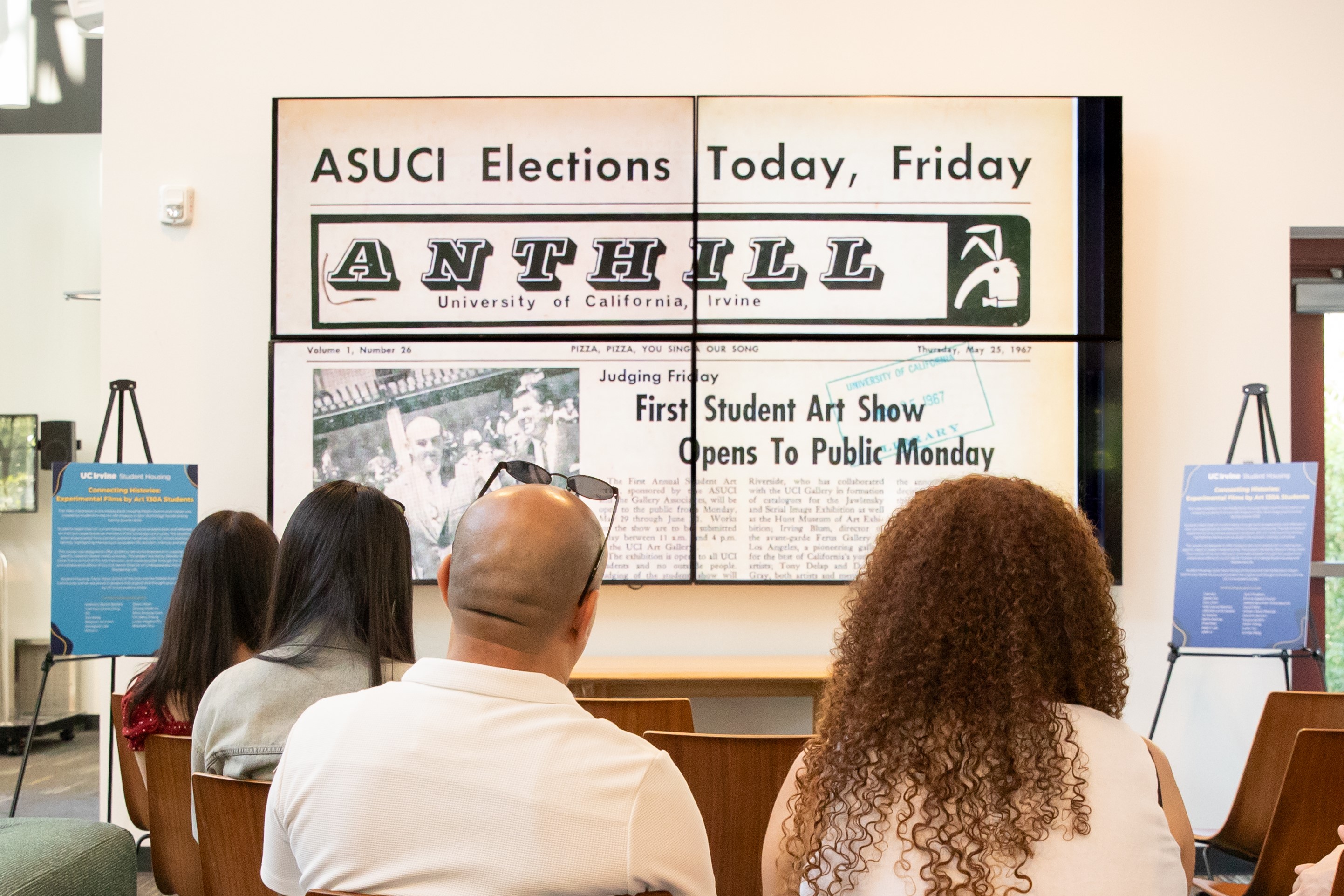 Audience members watch a student experimental film featuring archival images from UC Irvine’s history on a large video wall during the Connecting Histories exhibition.