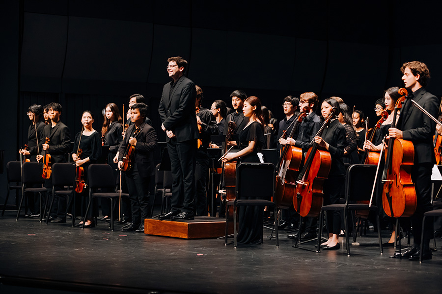 Geoffrey Pope and the UCI Symphony Orchestra take a bow on stage following a performance, with musicians standing beside their instruments.
