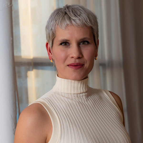 Boróka Nagy poses for a headshot in a cream turtleneck, backlit by soft window light