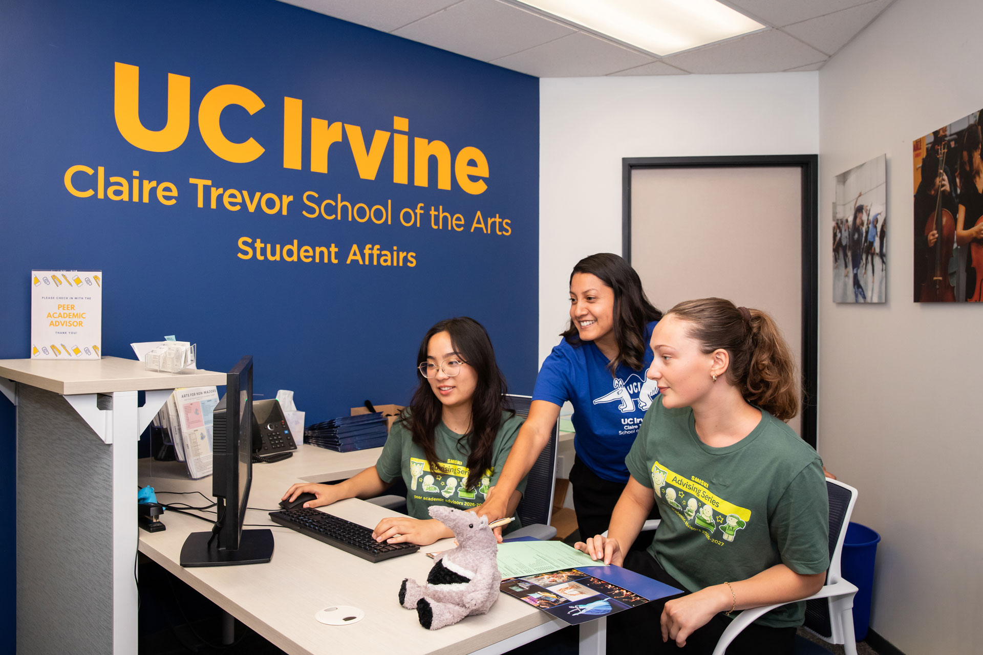 Three people work together at the UCI Claire Trevor School of the Arts Student Affairs reception desk.
