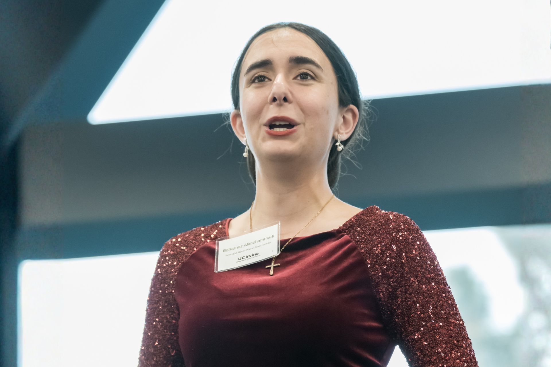 Baharnaz Alimohammadi, the Bette and Steven Warner Music Scholar, is singing, photographed from a low angle against an angular architectural backdrop.