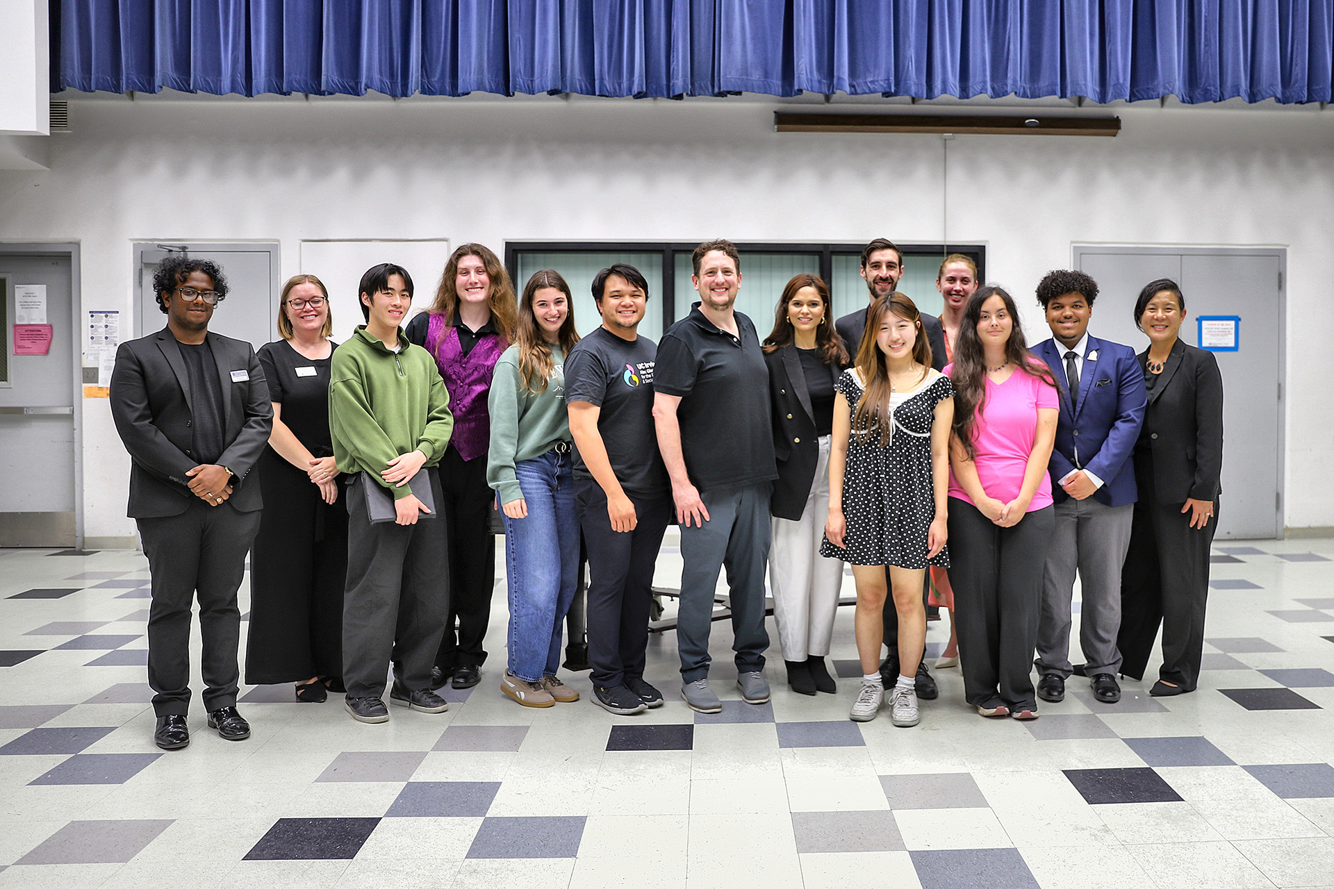 Larisa Martinez stands with a group of UC Irvine Claire Trevor School of the Arts students, faculty, and staff in a black-and-white checkered rehearsal hall, posing together for a group portrait.