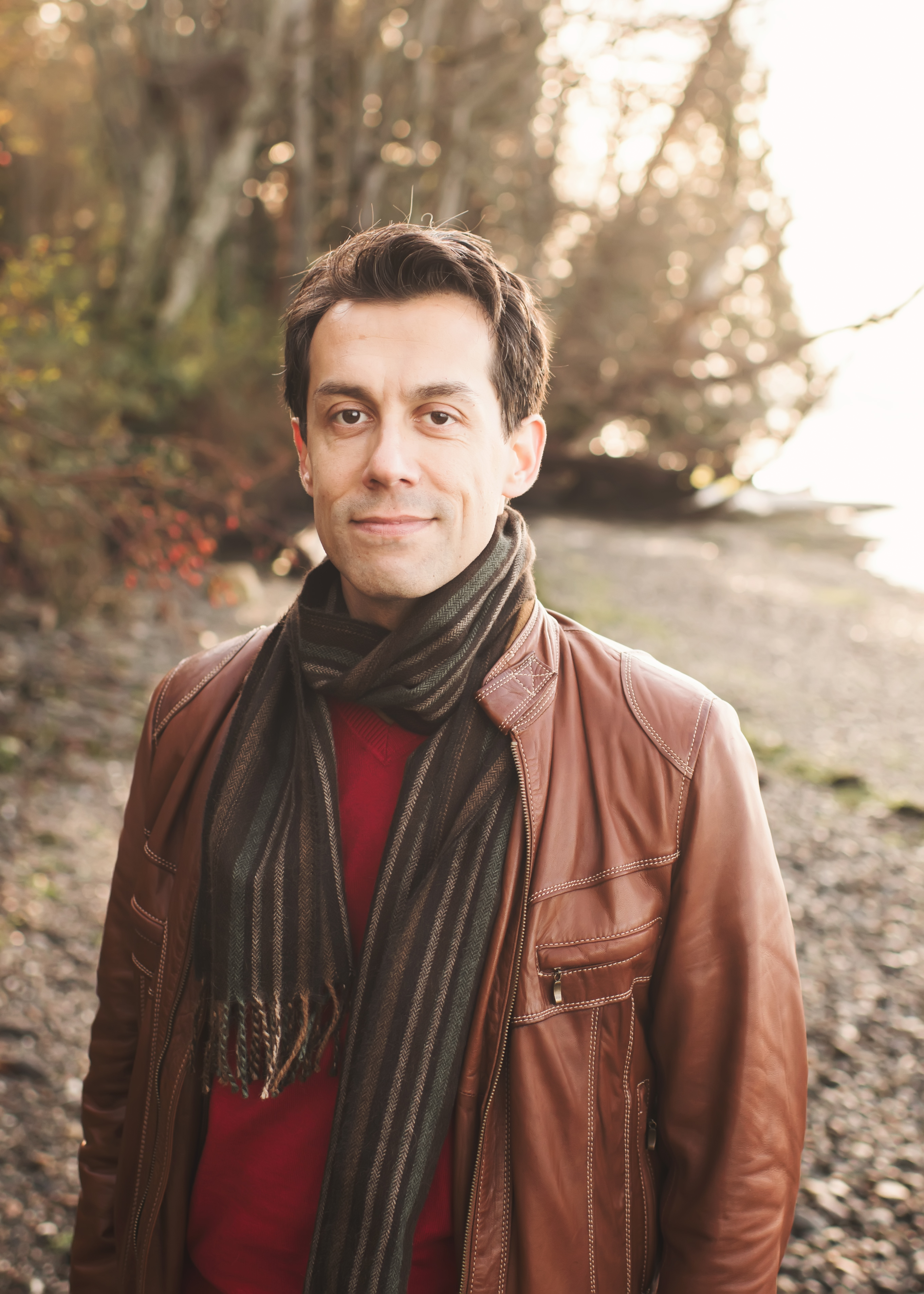 Person wears green neck scarf, red sweater, behind green foliage and rocks