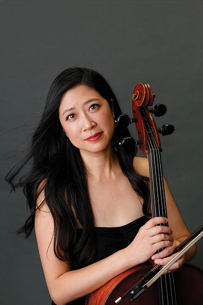 Sarah Koo Freeman poses with her cello against a gray backdrop.