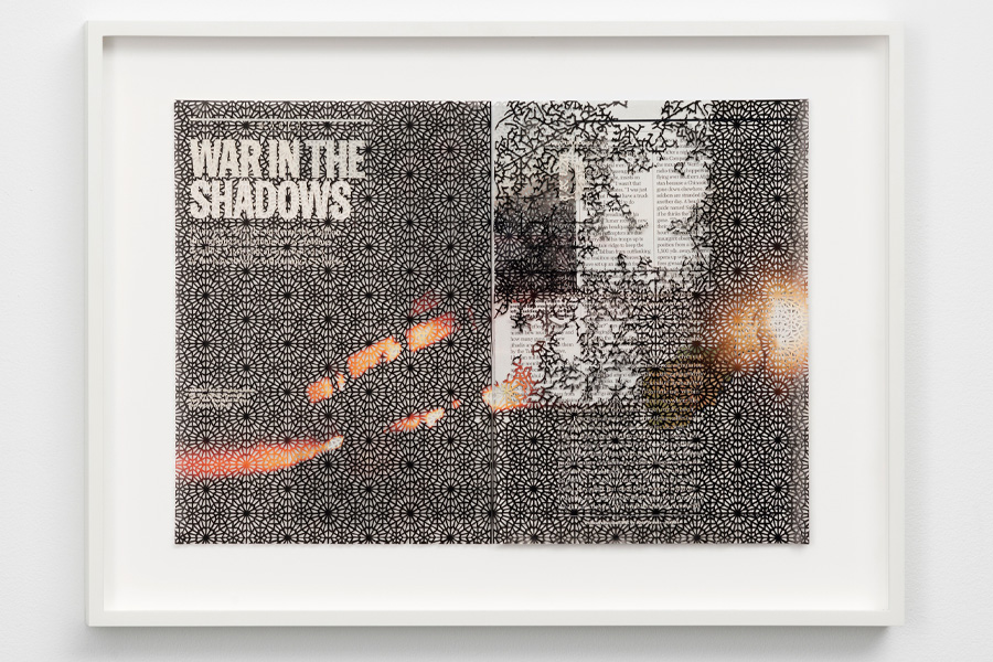 A framed work on paper made from a two-page magazine spread headlined “War in the Shadows,” overlaid with an intricate black lace-like cutout pattern that partially obscures the article text and an image of orange flames.