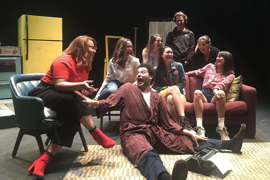 Image of actors on stage in an apartment setting, laughing and looking at each other on a couch