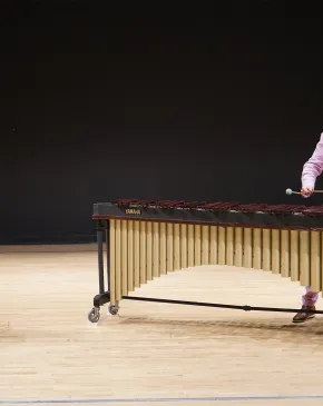 Two musicians perform on stage, with one playing the flute and the other playing a marimba in a formal concert setting.