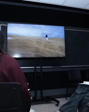 Students watch and discuss a video artwork displayed on a screen during a gallery viewing.
