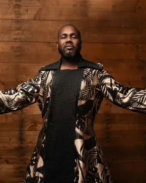 Kenneth Overton, a male vocalist, poses with his arms extended against a wooden backdrop.
