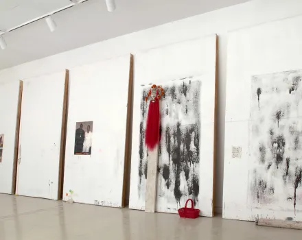 White gallery wall displaying large abstract black-and-white paintings mounted on wooden supports, with a red garment and red handbag incorporated into the installation.