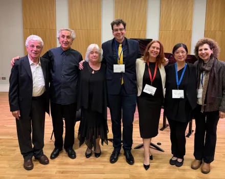 Seven people stand together smiling in a wood-paneled concert hall, several wearing conference lanyards and name badges