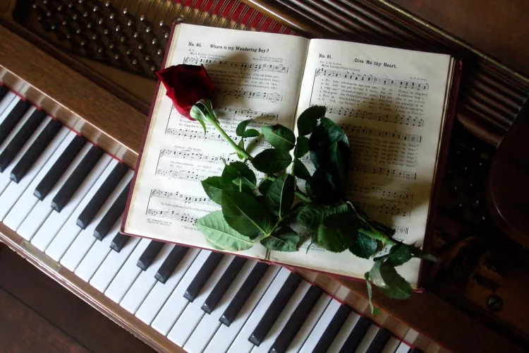 Red rose rests across open sheet music on the keys of a grand piano.