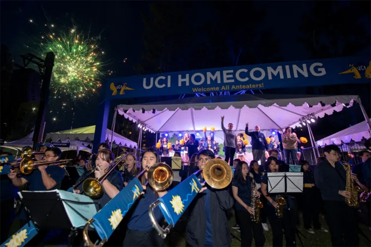 The UCI Athletics Band performs at Homecoming, playing in front of a stage as fireworks light up the night sky.