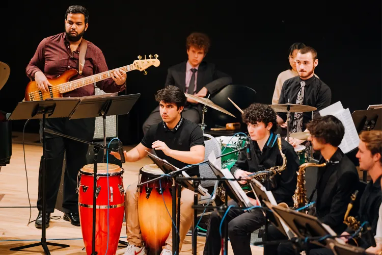 A student jazz ensemble performs on stage, featuring bass, percussion, drums, and saxophone.