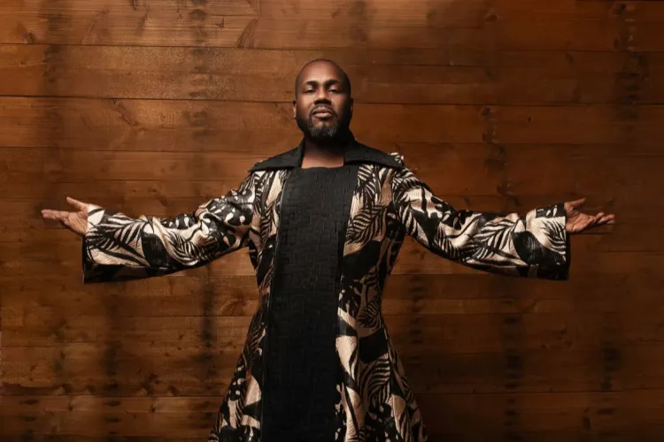 Kenneth Overton, a male vocalist, poses with his arms extended against a wooden backdrop.