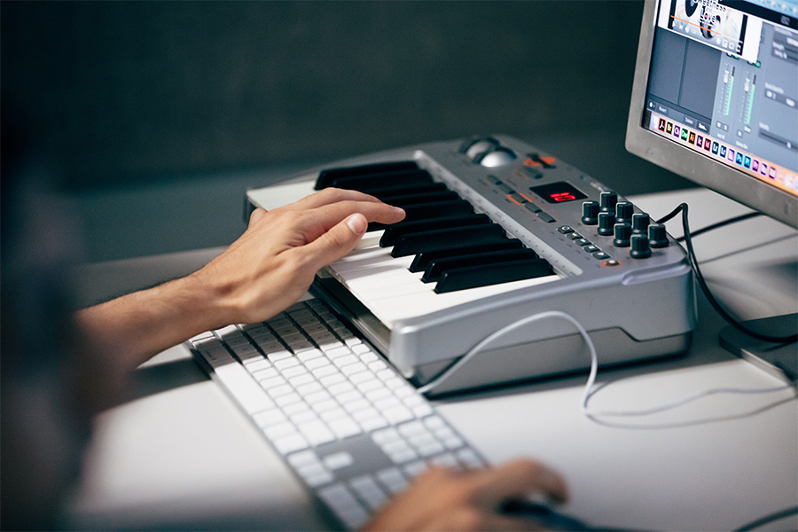 Close up image of hands playing a portable electric keyboard and holding a computer mouse on a desk