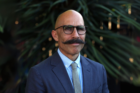 Person in glasses and mustache in front of foliage