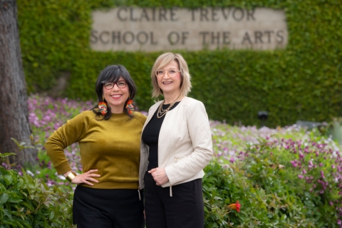 Sara Guerrero and Tiffany Ana López stand in front of the ivy covered Claire Trevor School sign