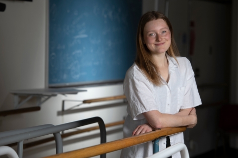 Student Veroinca Allen stands at a dance bar in one of the studios with a chalkboard in the backgrou