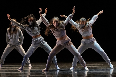 Dancers aligned on stage with arms and legs outstretched